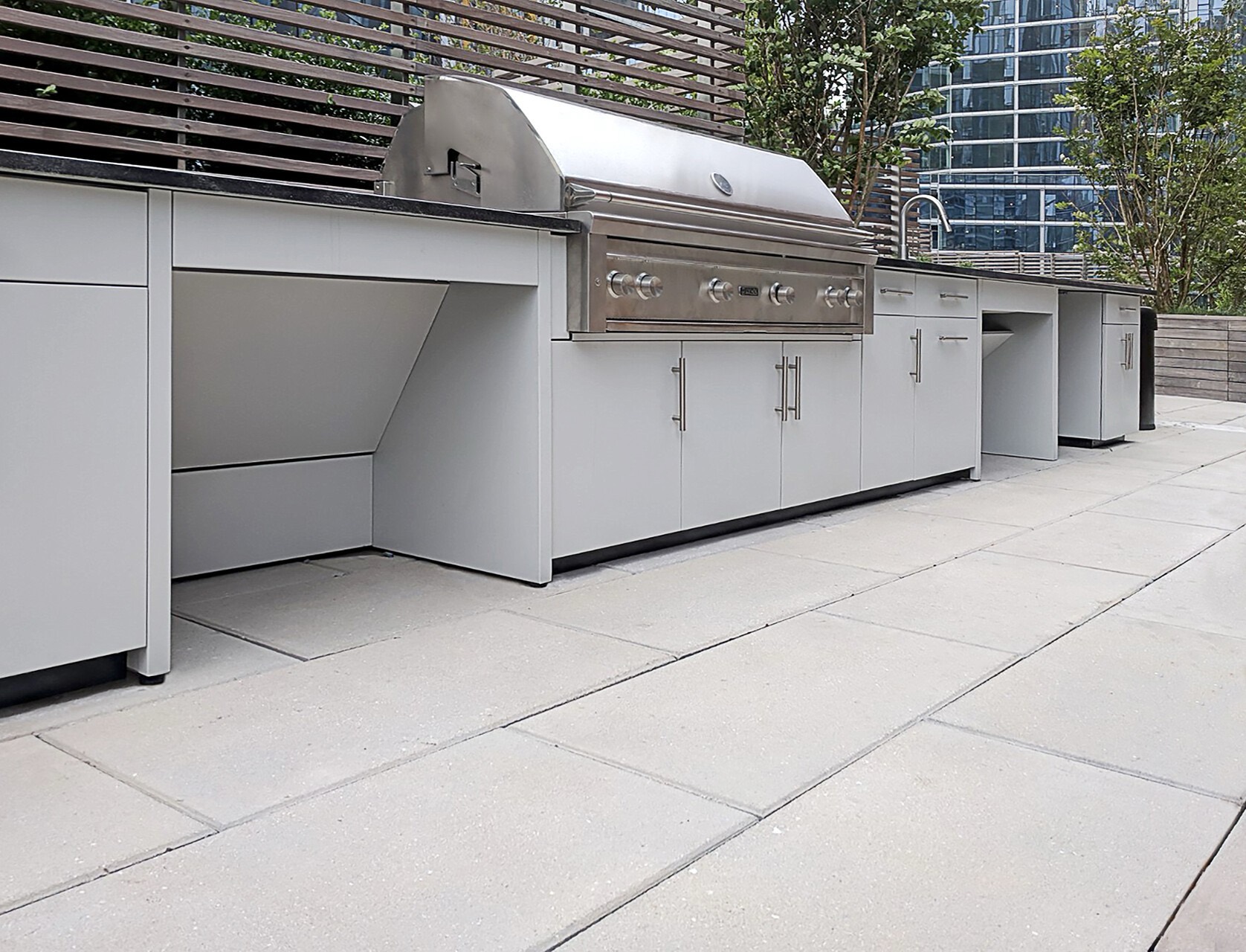 White outdoor kitchen on a city rooftop with open roll-under bays for wheelchair access beside a large stainless grill