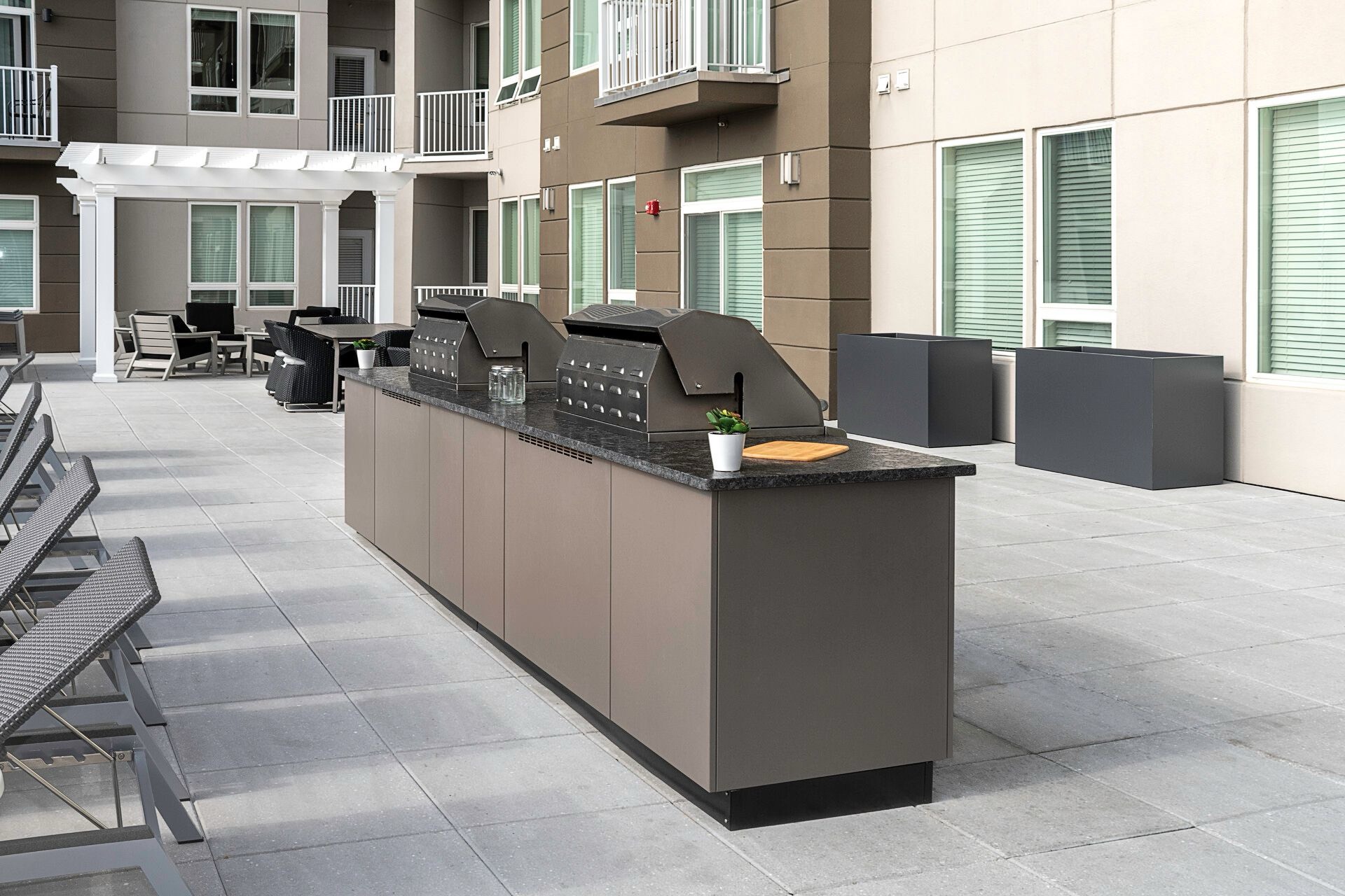Taupe outdoor kitchen with two grills and a granite top in an apartment courtyard beside lounge chairs