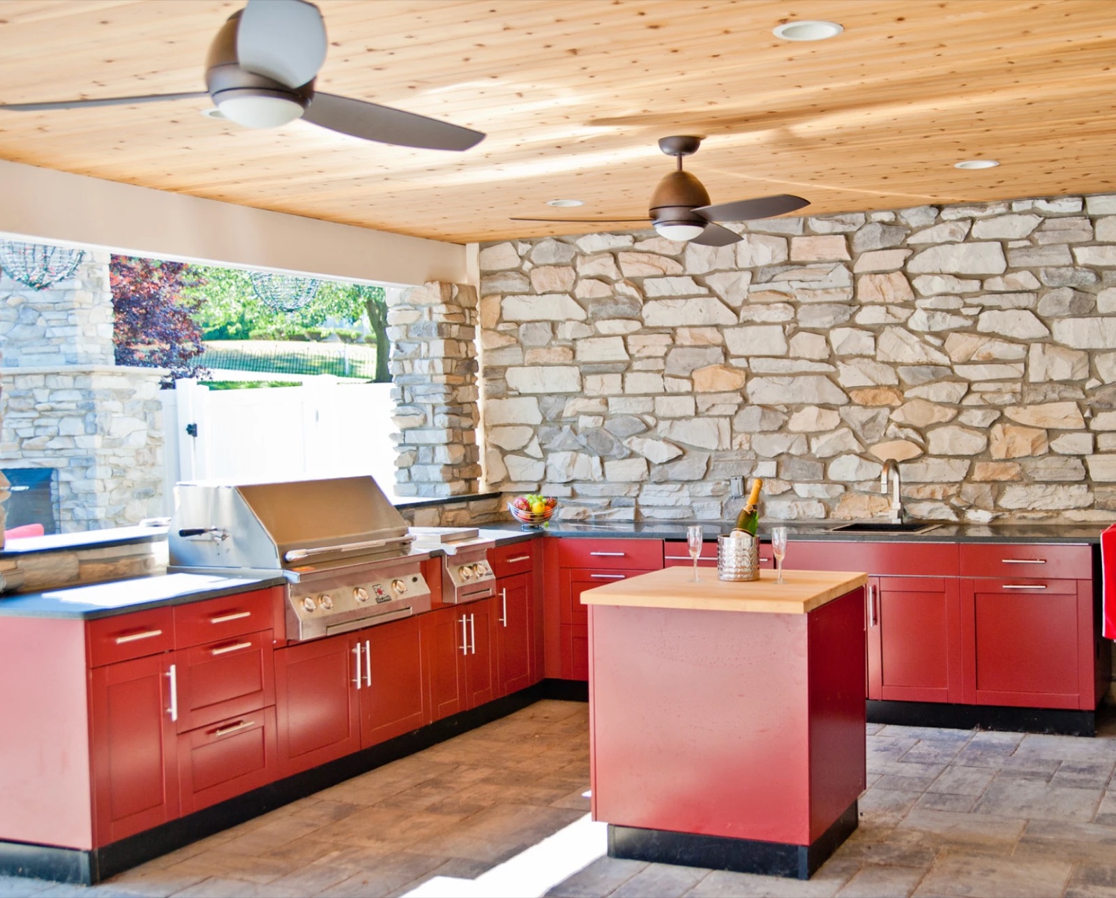Red outdoor cabinets with a butcher-block island under a covered cedar ceiling