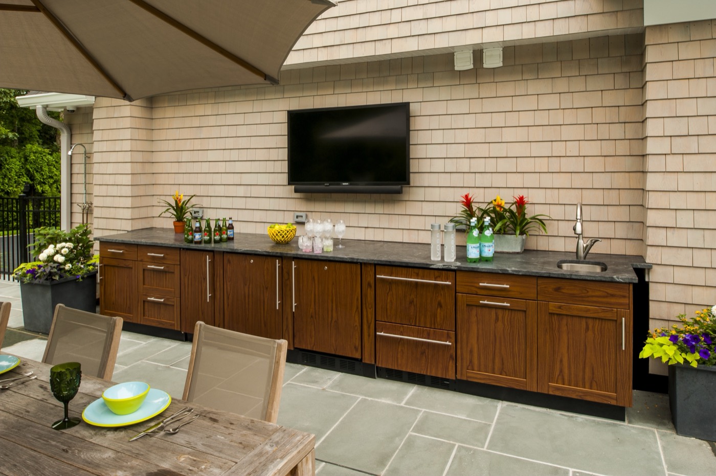 Wood-grain outdoor cabinets under a television on a stone patio