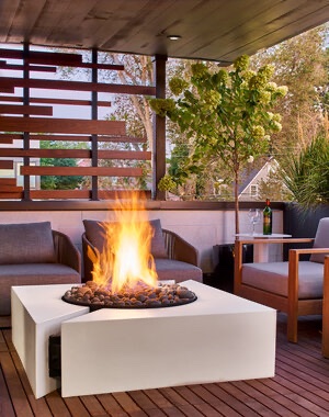 White block-shaped Chaos concrete firepit burning on a covered wood deck at dusk
