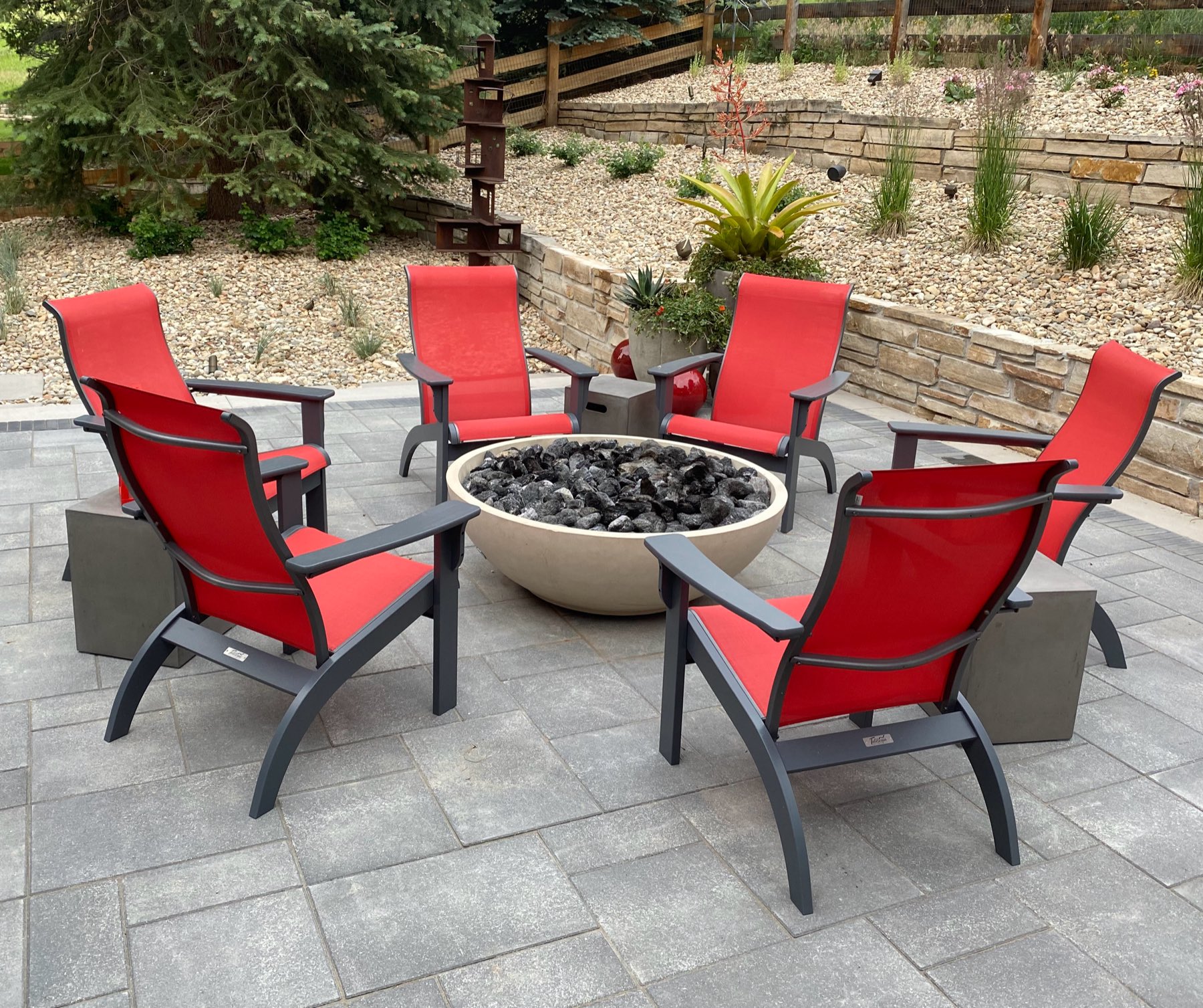 Round Palmer concrete firepit bowl surrounded by red lounge chairs on a stone patio
