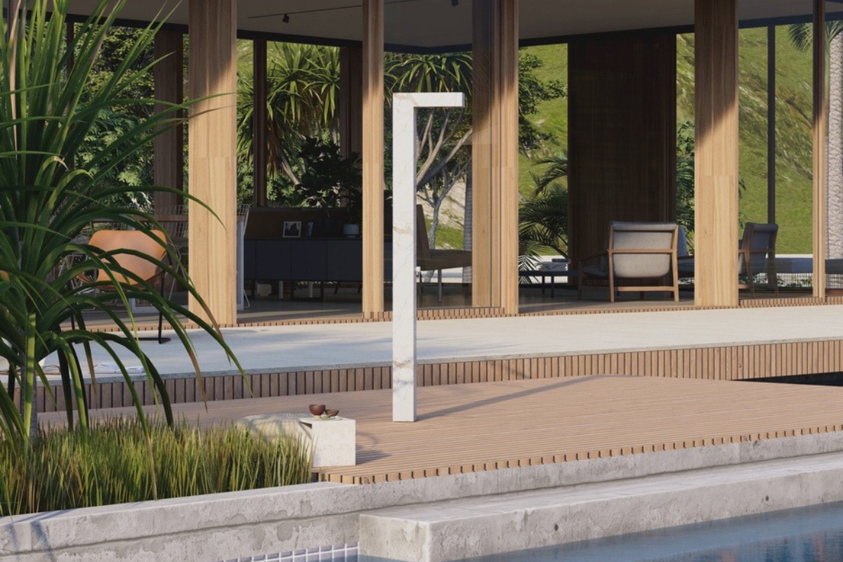 Slim white Korta column shower on a wood pool deck beside tropical planting