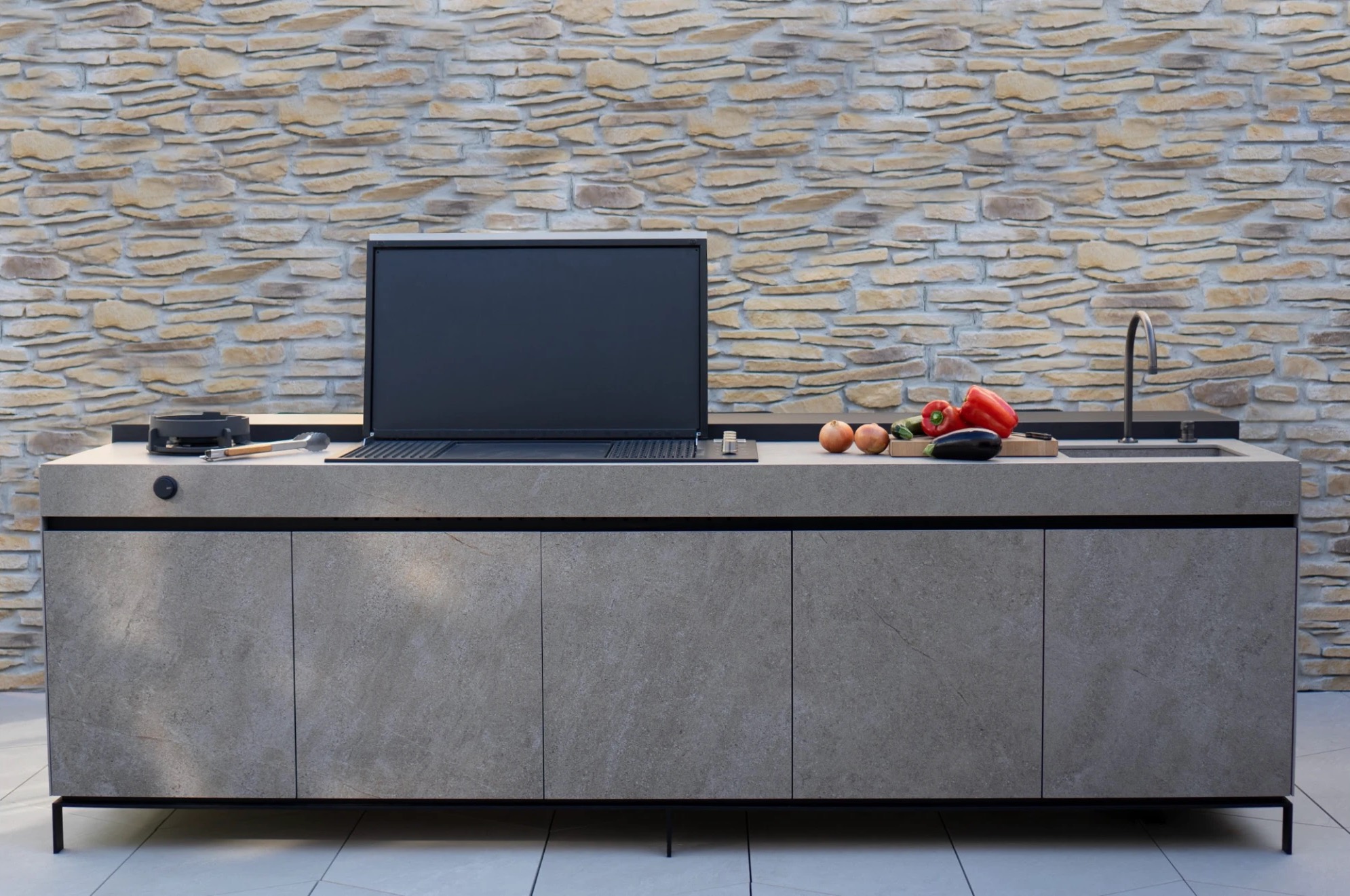Grey stone-look Novara kitchen with a built-in grill and sink against a stacked stone wall